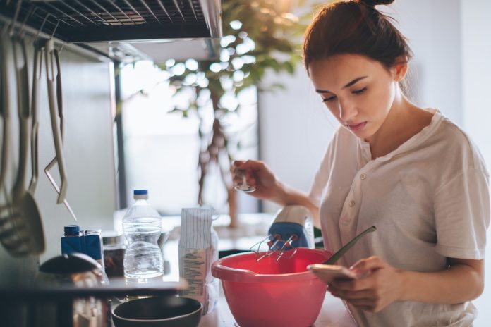 Young woman in the kitchen, reading recipe from the internet