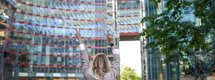 Corporate people. Rear view of businesswoman raising hands up in celebration, triumphing, achieve goal and rejoicing, standing on street